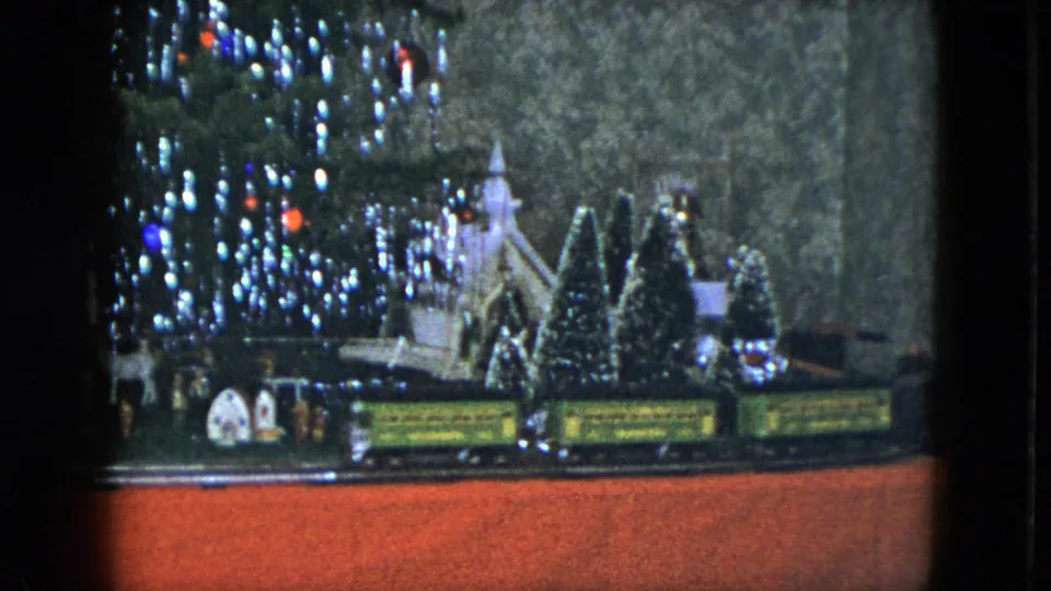 1951 Cleveland 8mm frame showing model train cars in front of a miniature church, small evergreens, tree lights, and red storefront display floor.