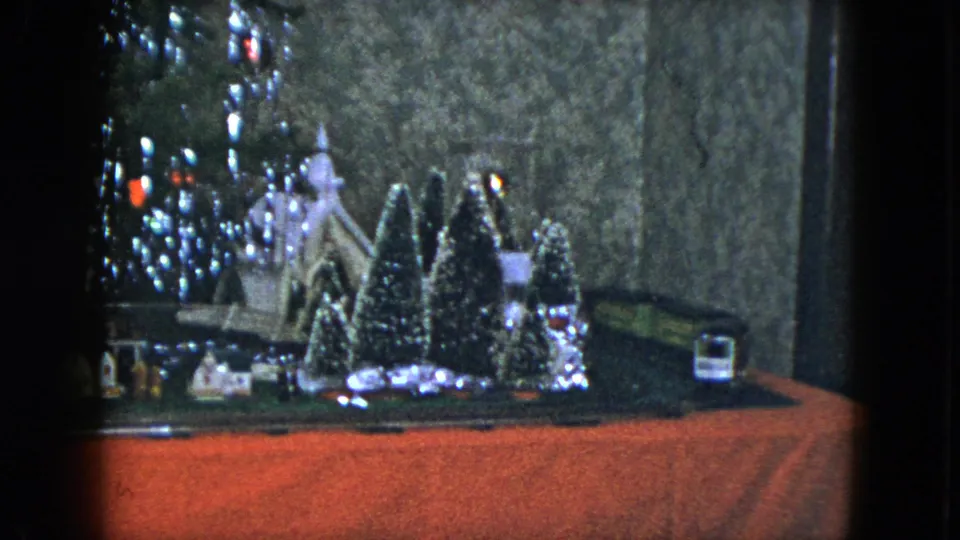1951 Cleveland storefront holiday scene with miniature church, evergreen trees, lit Christmas tree edge, train track, red floor, and a small vehicle-like object.