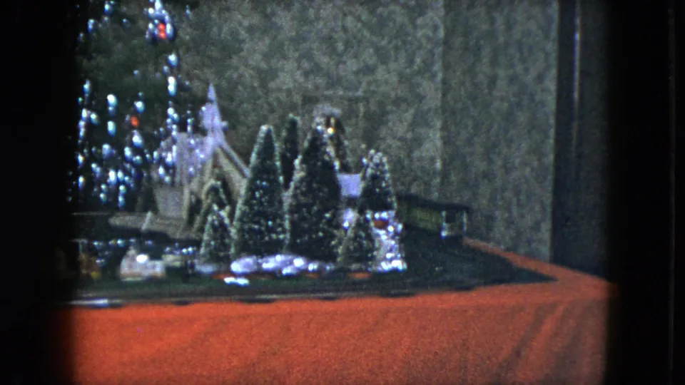1951 Cleveland 8mm frame showing a model train display with small houses, snow-dusted trees, tinsel lights, and red base cloth.