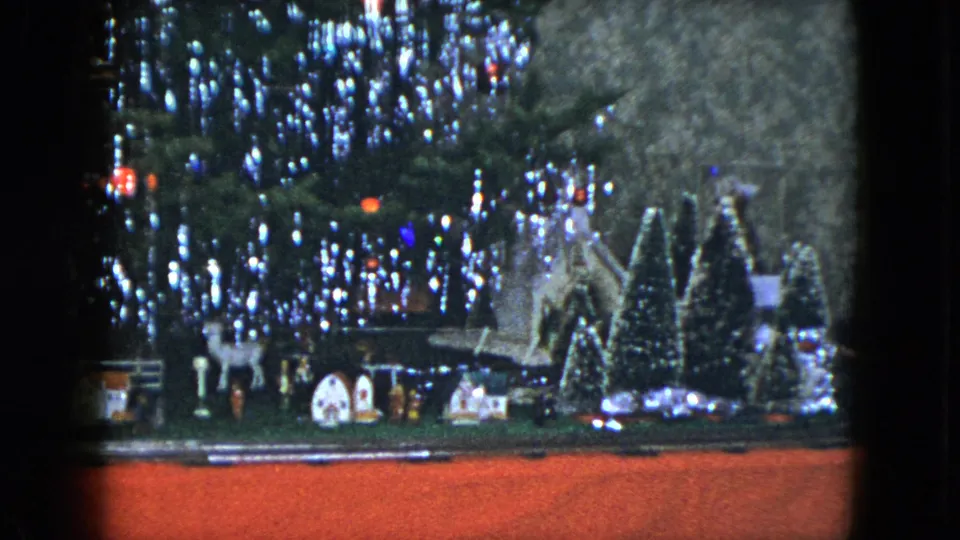 1951 Cleveland 8mm still showing a tabletop-style Christmas village, train track, small buildings, and bright tree lights.