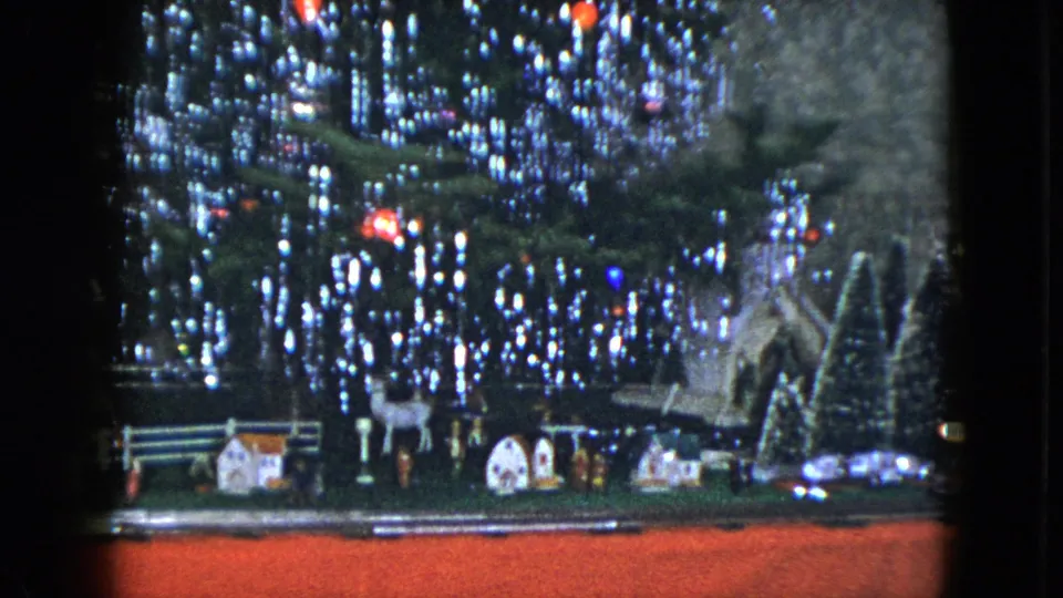 1951 Cleveland home-movie frame showing a wider Christmas train village with miniature houses, figures, trees, and red display base.