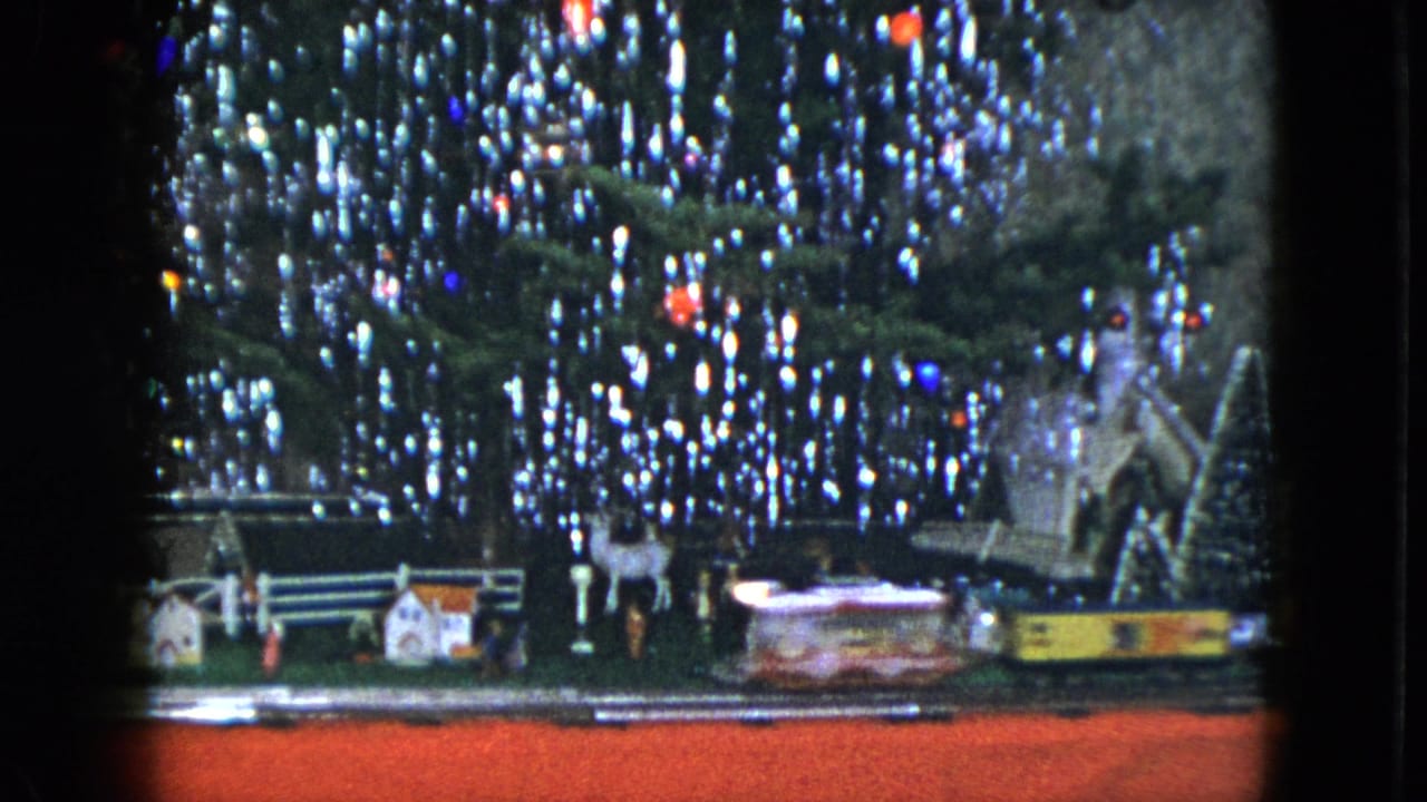 Toy train display beneath sparkling Christmas lights with miniature houses and deer figures.