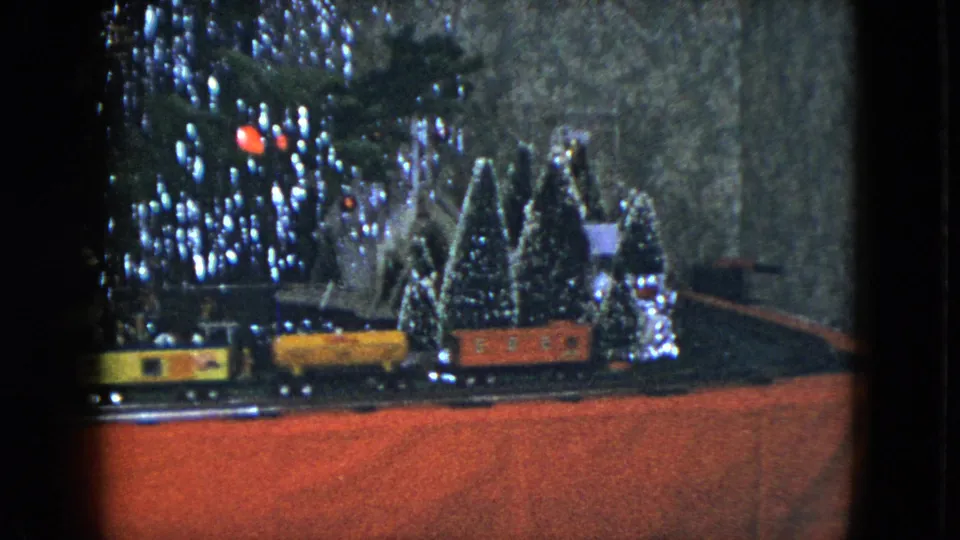 The final frame shows the holiday train set with yellow and orange cars, small evergreens, houses, and bright tree lights.