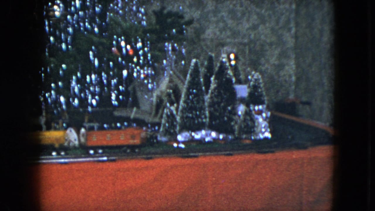 1951 Cleveland 8mm frame of a red model train near a lit Christmas tree and miniature holiday village display.