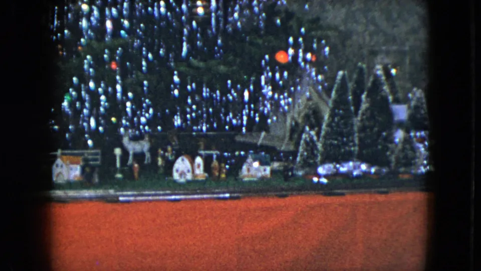 1951 Cleveland 8mm view of a Christmas tree base with model train track, small houses, deer figures, and snowy trees.