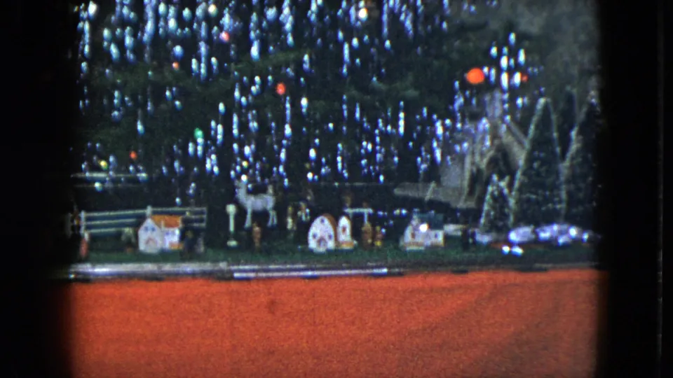 1951 Cleveland home-movie frame showing the Christmas tree base, model train track, miniature houses, white deer, and snowy display pieces.