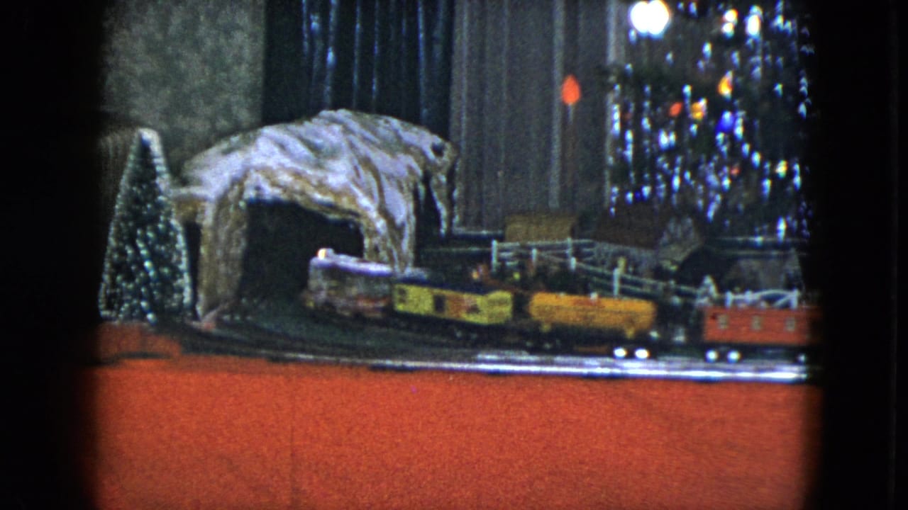 1951 Cleveland home-movie frame showing a tabletop Christmas train layout with a tunnel, miniature trees and reflective holiday decoration.