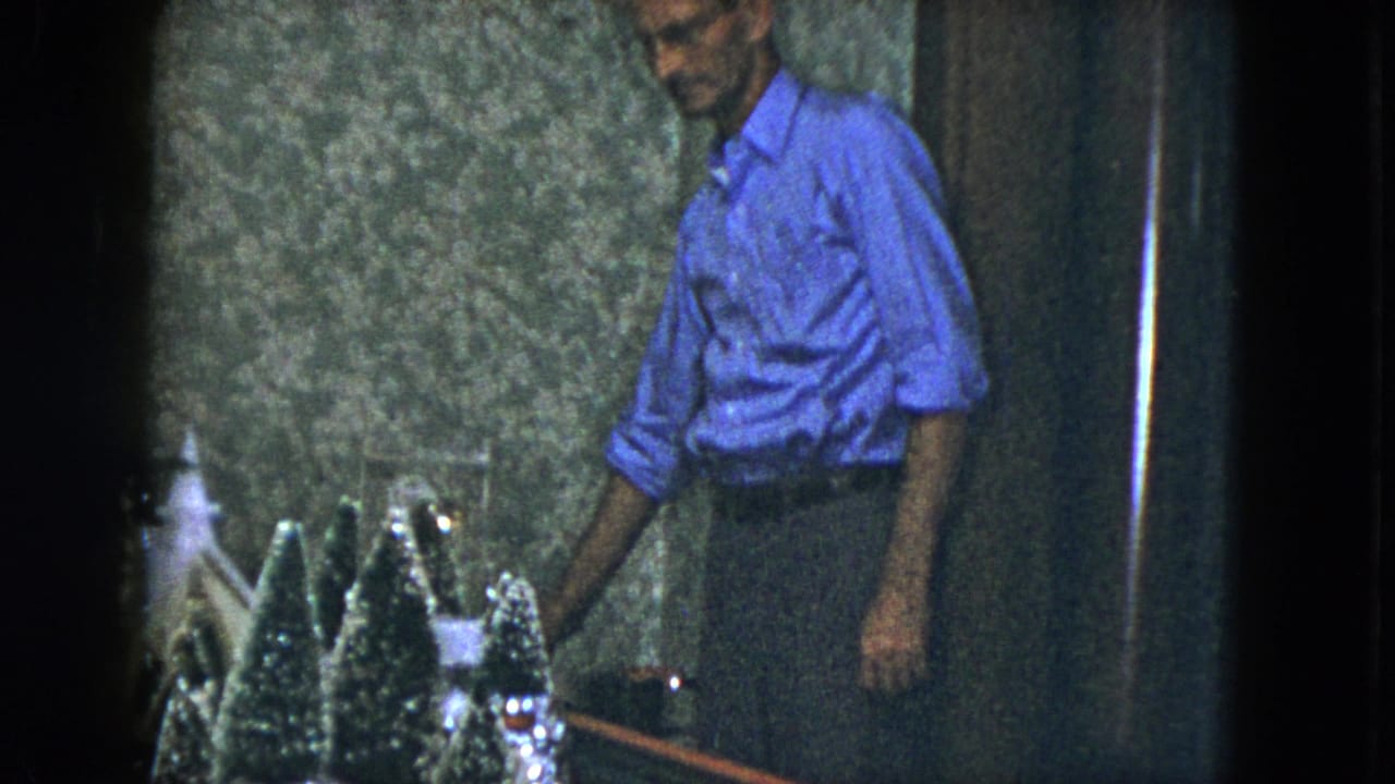 In a 1951 Cleveland home interior, a man in a blue shirt stands near a table with miniature Christmas decorations.