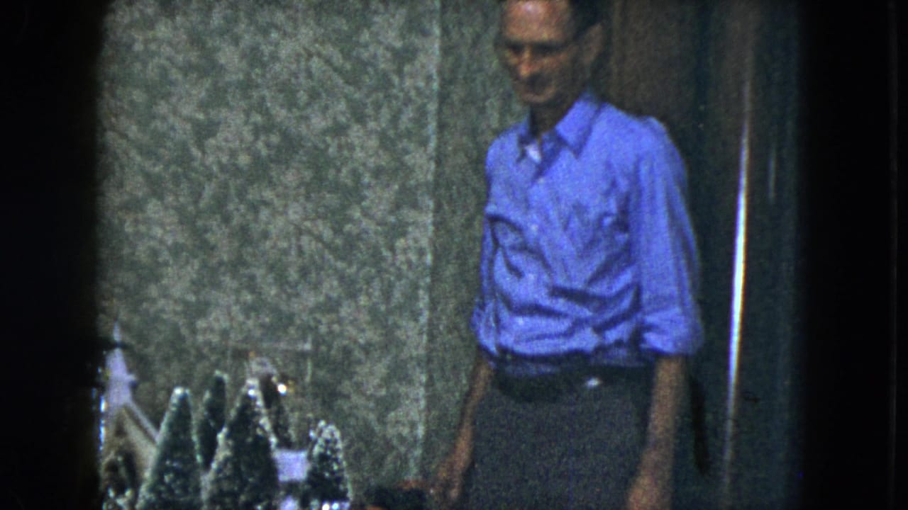 Man stands near a tabletop display of small Christmas trees.