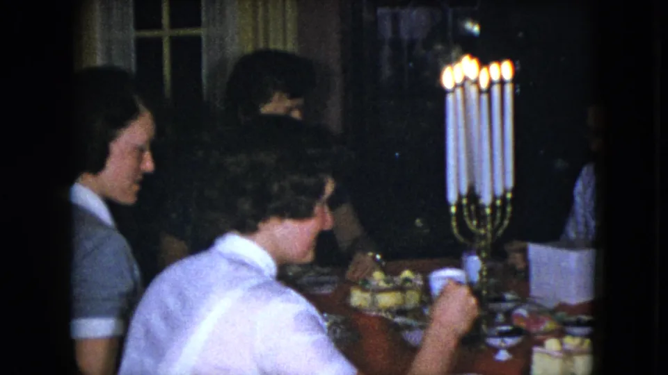 A candlelit family dinner appears inside a private Cleveland home, with women seated around the table in 1951 footage.