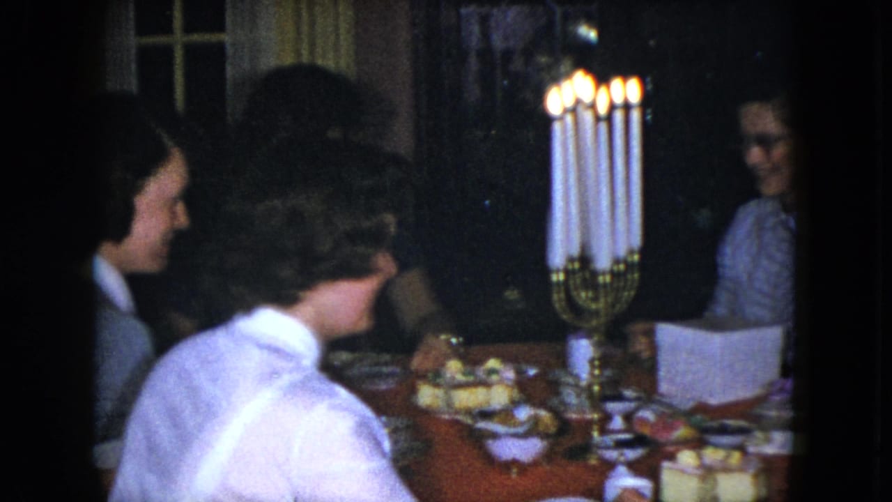 1951 Cleveland home-movie frame showing adults gathered at a dinner table near tall lit candles and serving dishes.