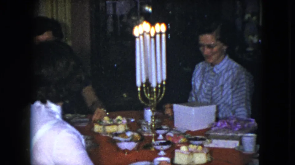 1951 Cleveland frame of a woman in a striped blouse seated at a candlelit dinner table in a private interior.