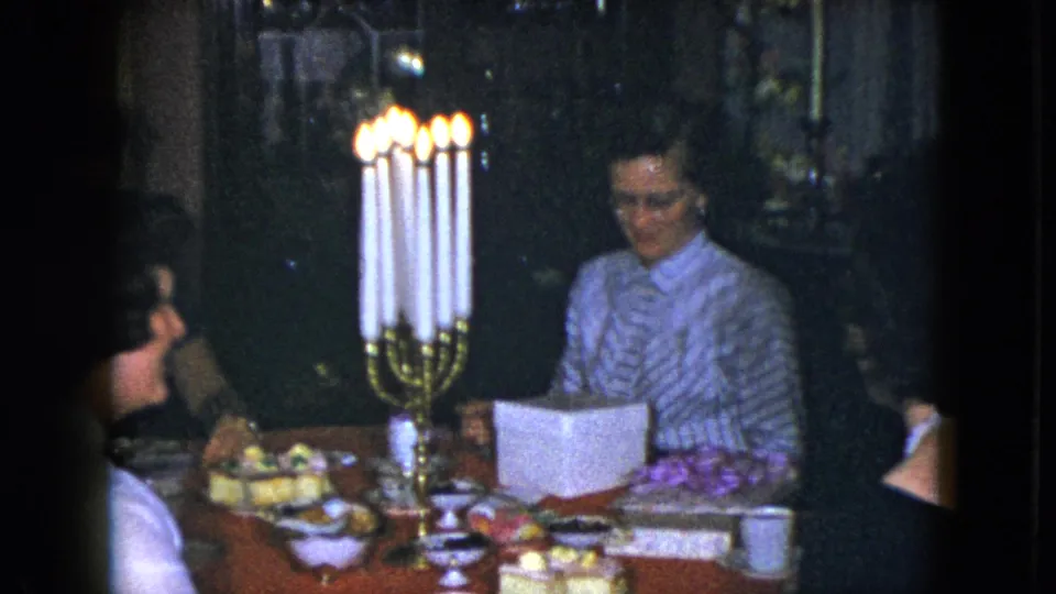 1951 Cleveland home-movie frame with several adults around a candlelit dinner table and a woman facing camera.