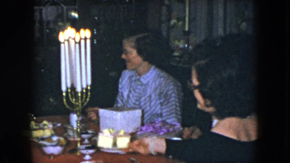 1951 Cleveland frame showing a woman looking toward another guest beside tall candles and plated dessert pieces.