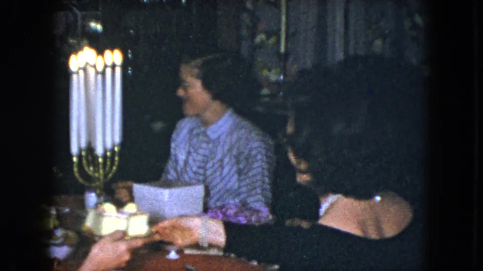 In Cleveland 1951 home-movie footage, two adult women sit beside a tall lit candelabra at a dining table.
