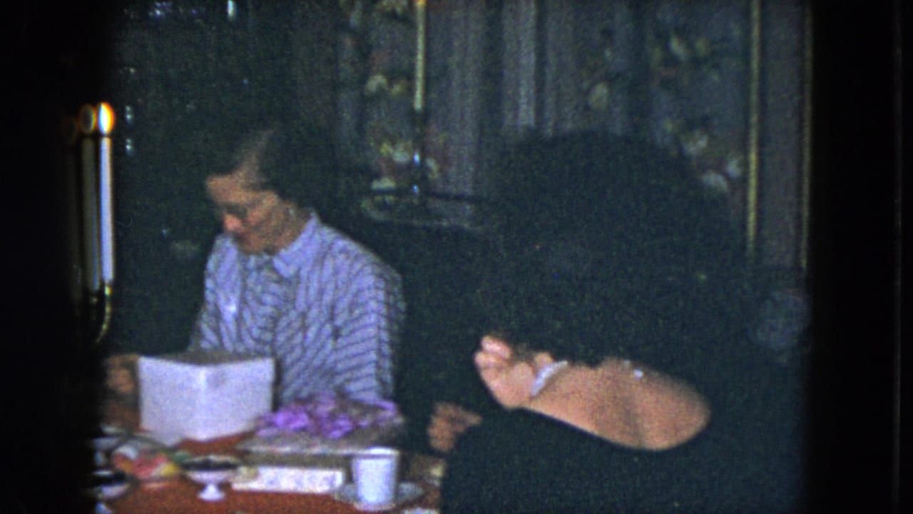 A woman in a striped blouse sits at a candlelit table while another adult woman in a dark dress faces down nearby.
