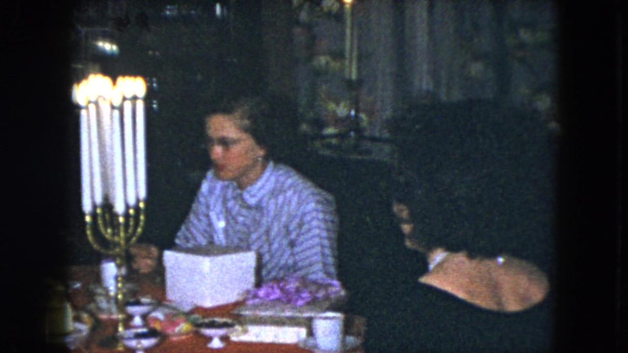 A woman in a striped blouse sits beside a tall lit candelabra at a dining table.