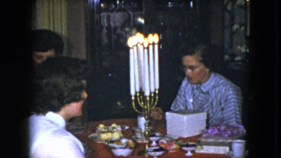 1951 Cleveland home-movie frame of several guests around a red dining table with candles, food, flowers, and a white box.