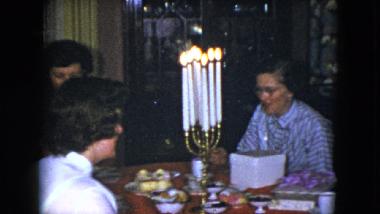 Several women sit around a candlelit table with food and a white box.