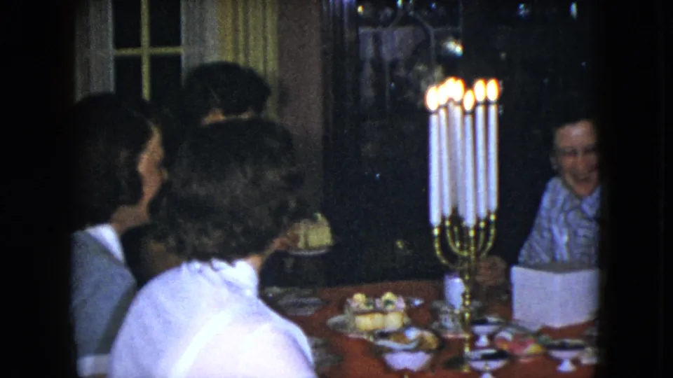 1951 Cleveland home interior frame with women gathered closely around a candlelit table with food and cups.