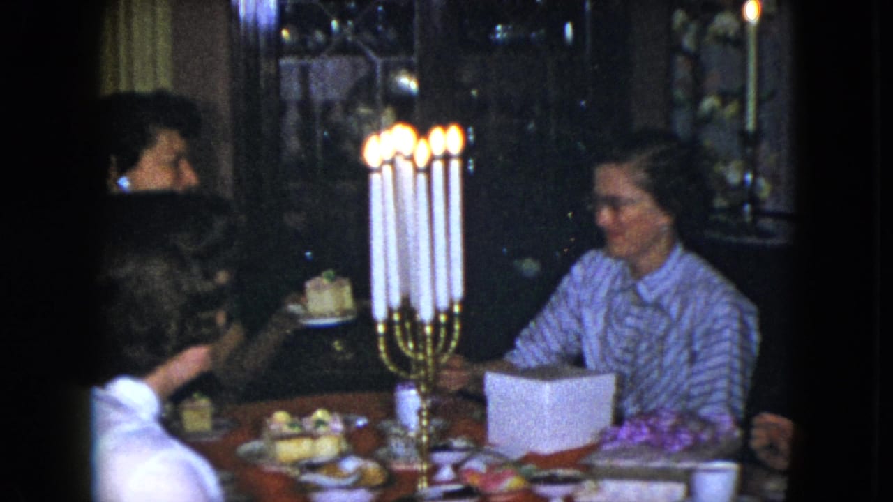 1951 Cleveland home-movie frame showing women around a dim dining table with a tall lit candelabra and plates of food.