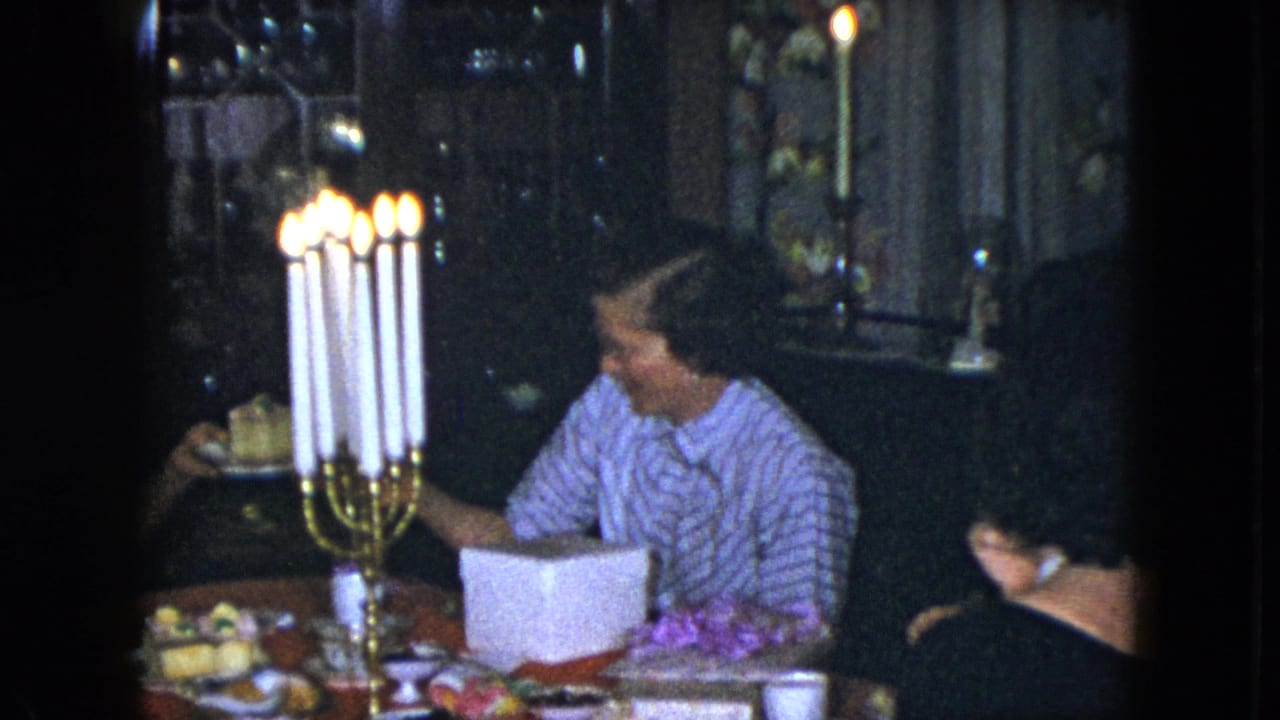 A woman reaches across a candlelit table while others sit nearby.