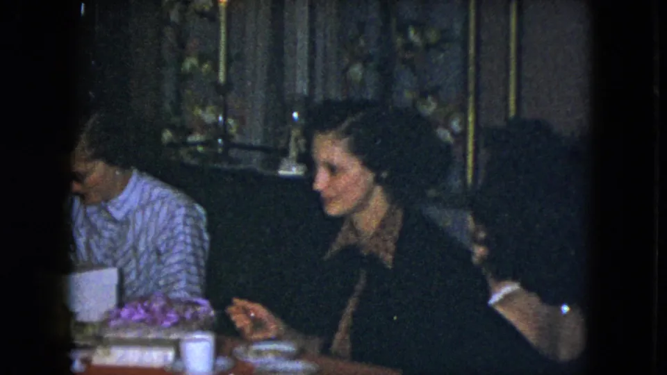 1951 Cleveland home-movie frame showing women at a dim indoor meal with tableware, desserts, and candlelight.