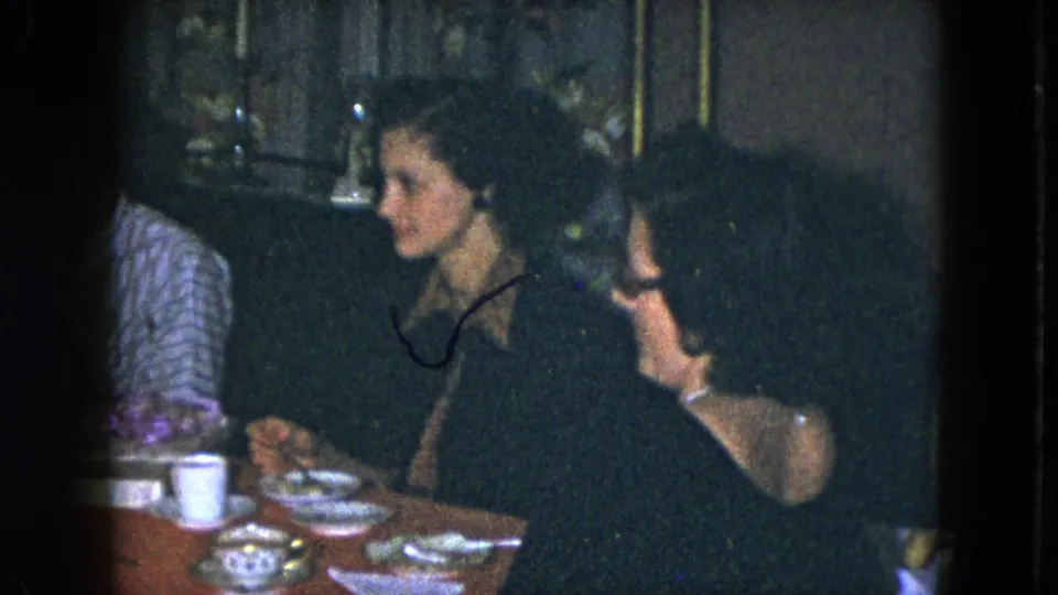 1951 Cleveland home-movie frame of women in conversation at a dining table with tea service and small dishes visible.