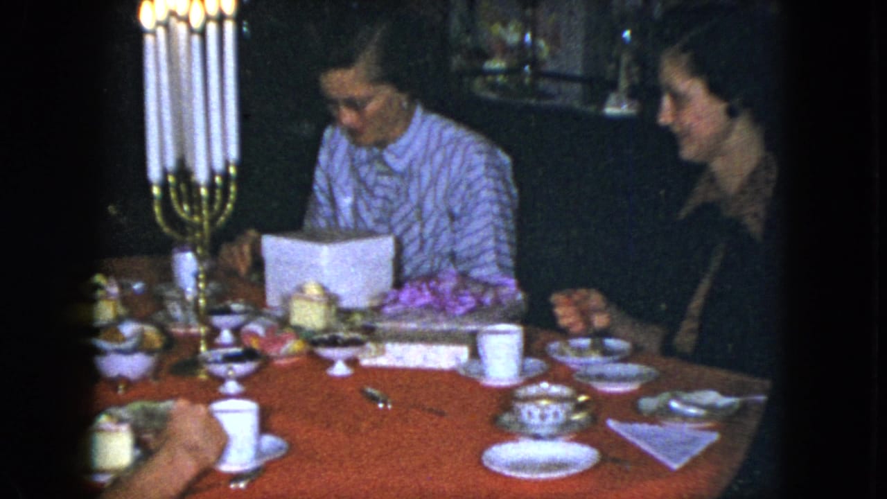 A Cleveland 1951 birthday gathering shows a woman in a striped blouse looking into a white gift box beside cups, plates, and candles.