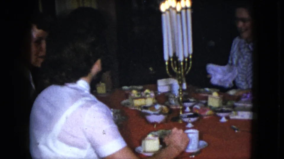 1951 Cleveland home-movie view across a dim dinner table with adults, dessert plates, and tall lit candles.