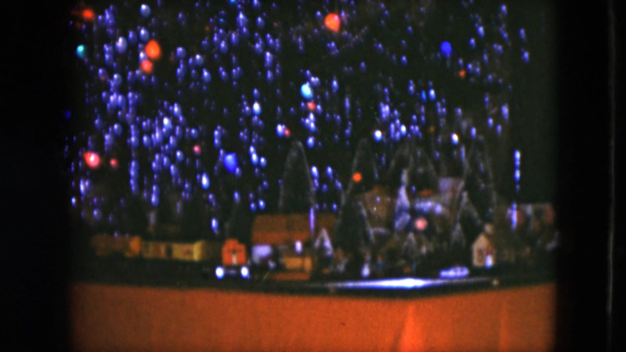1951 Cleveland home-movie frame showing colored Christmas tree lights over a tabletop model railway and small houses.