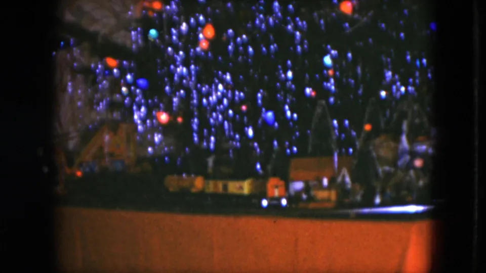 The home-movie view lingers on a tabletop toy train scene below the illuminated Christmas tree.
