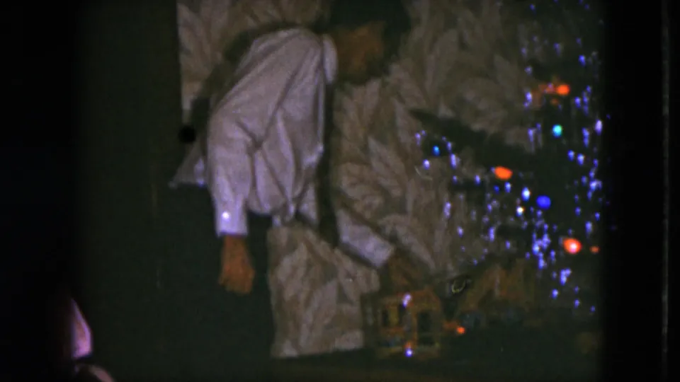 In a 1951 Cleveland home movie, a man in a white shirt and tie bends toward a model train set under a tinsel-covered Christmas tree.