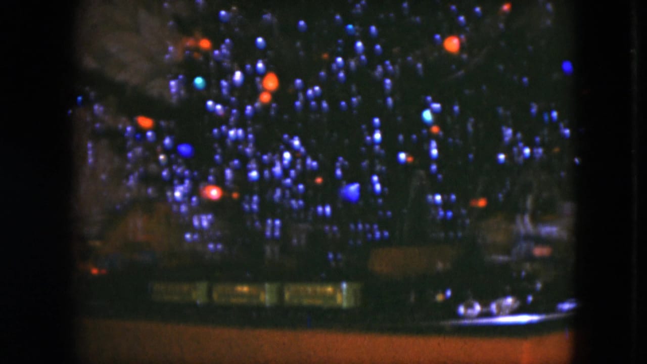 1951 Cleveland 8mm frame with a lit Christmas tree and toy train layout seen from a steady indoor viewpoint.