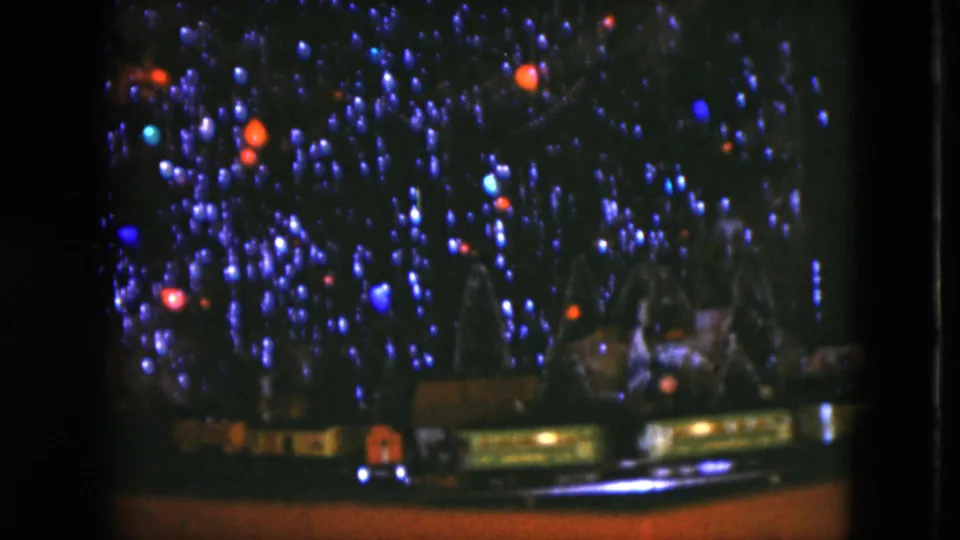 1951 Cleveland home-movie still showing dense Christmas lights above a toy train scene inside a private room.