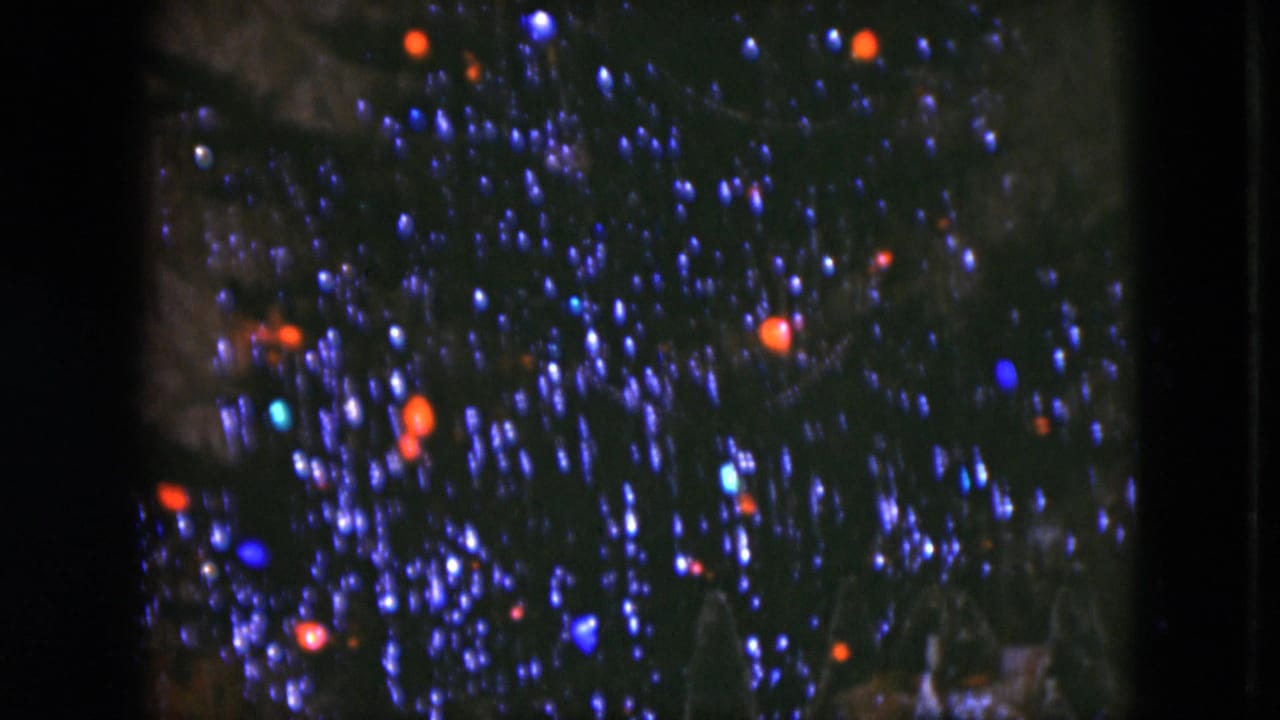 1951 Cleveland home-movie frame showing a tinsel-covered Christmas tree with red and blue lights glowing in soft focus.