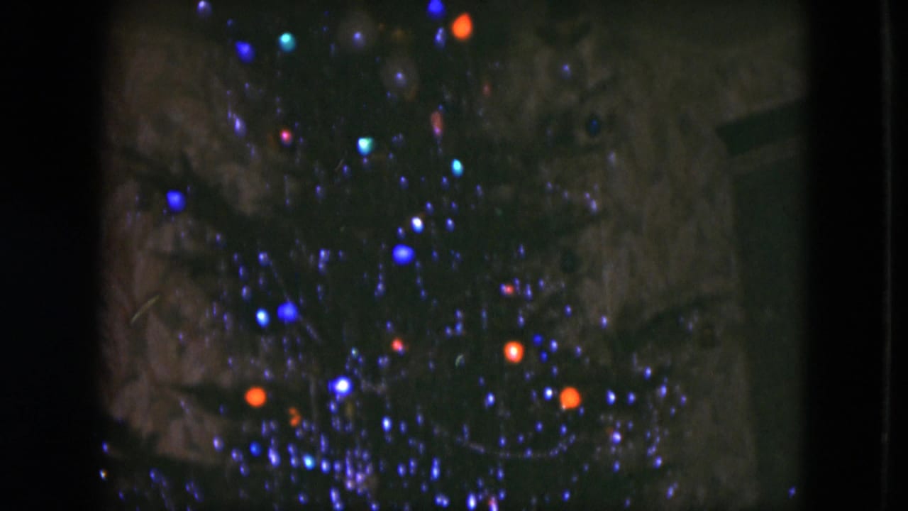 1951 Cleveland home-movie frame showing blue and orange Christmas tree lights against dark evergreen branches.