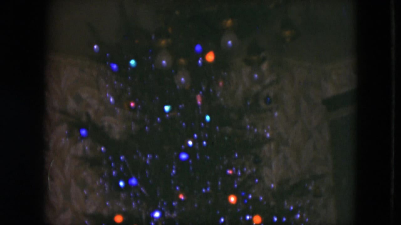 Close 8mm view of blue, orange, and small cyan Christmas lights on a dark tree in Cleveland, 1951.
