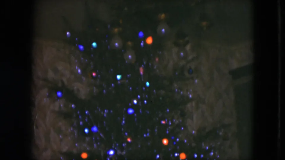 Close 8mm view of blue, orange, and small cyan Christmas lights on a dark tree in Cleveland, 1951.