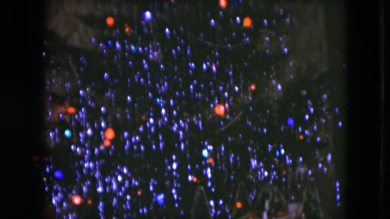 1951 Cleveland home-movie frame showing a dark Christmas tree with glowing colored bulbs and a partial miniature display below.