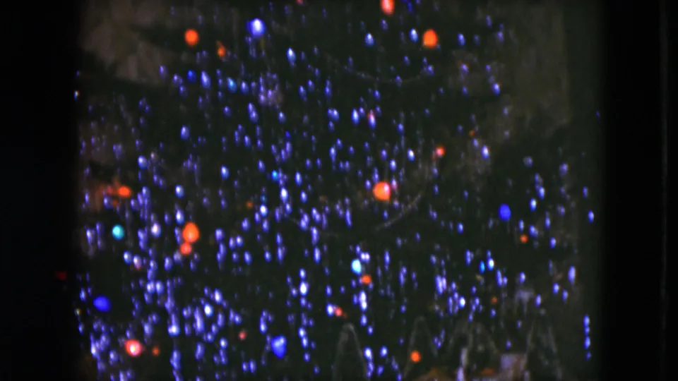 1951 Cleveland home-movie frame showing a dark Christmas tree with glowing colored bulbs and a partial miniature display below.