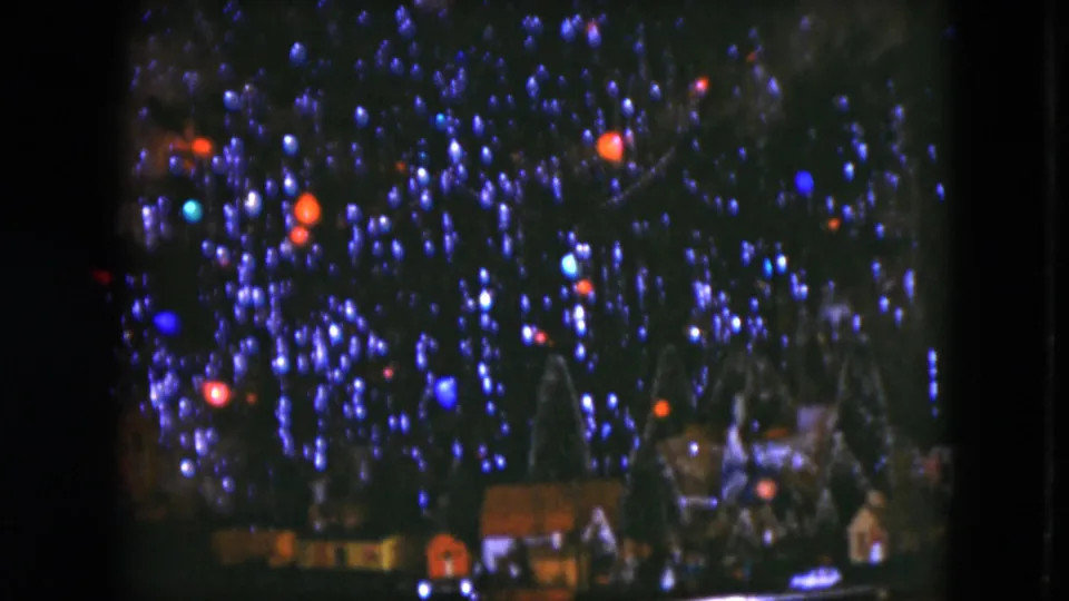 1951 Cleveland 8mm frame of glowing Christmas bulbs with a miniature holiday village and train-set scenery at the tree base.