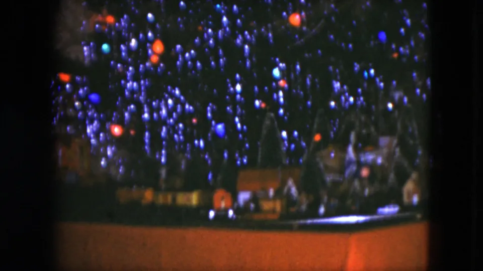 1951 Cleveland home-movie view of a Christmas tree base with a model train village, small houses, trees, and glowing bulbs above.