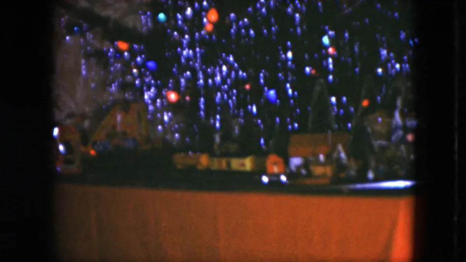 1951 Cleveland 8mm frame showing the base of a Christmas tree with colored lights, miniature houses, model trees, and train-set layout details.