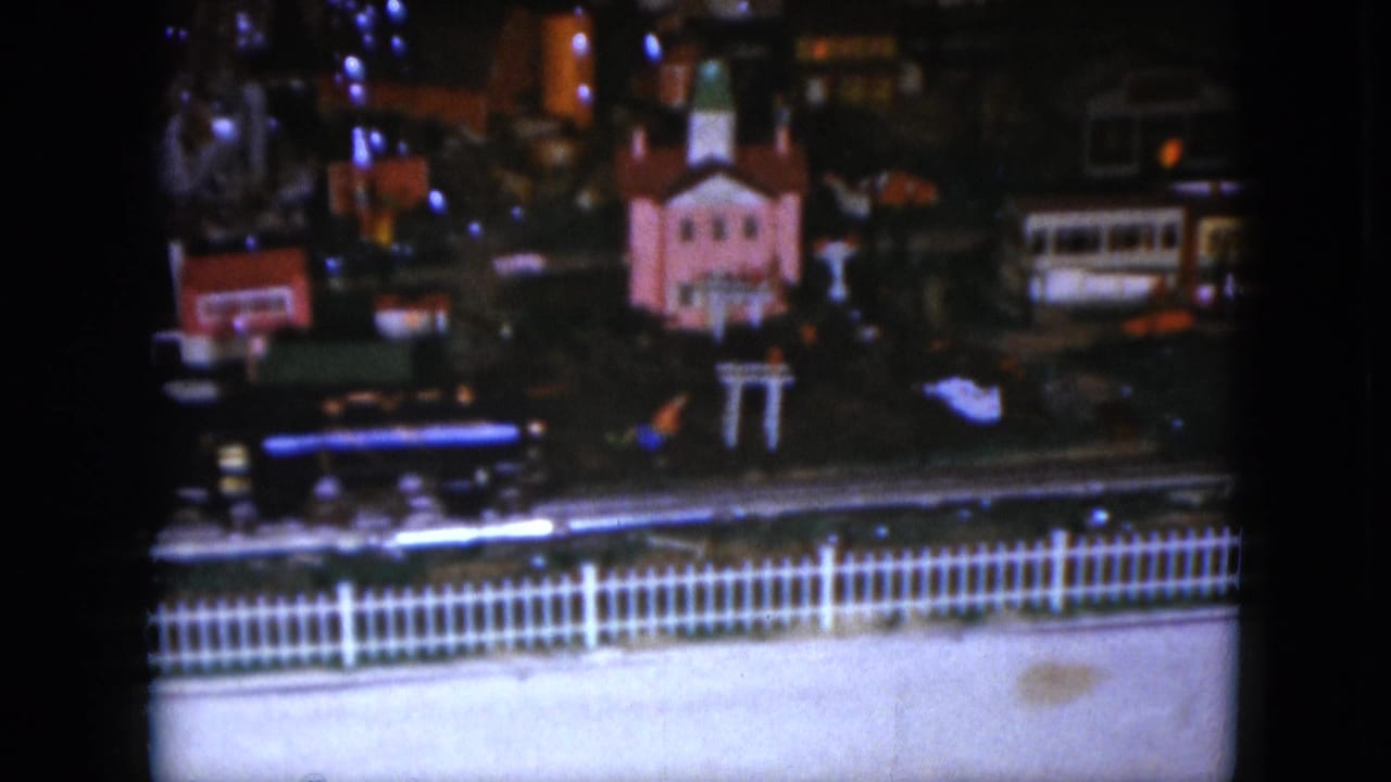 Toy train display with a pink church-like miniature, track, and white picket fence in front.