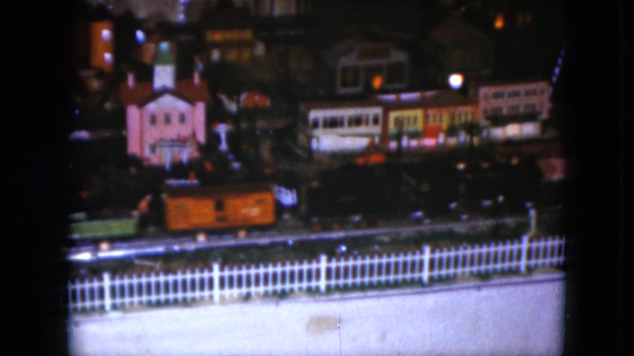 1951 Cleveland 8mm frame with an orange toy rail car moving past small lit buildings in a miniature village display.