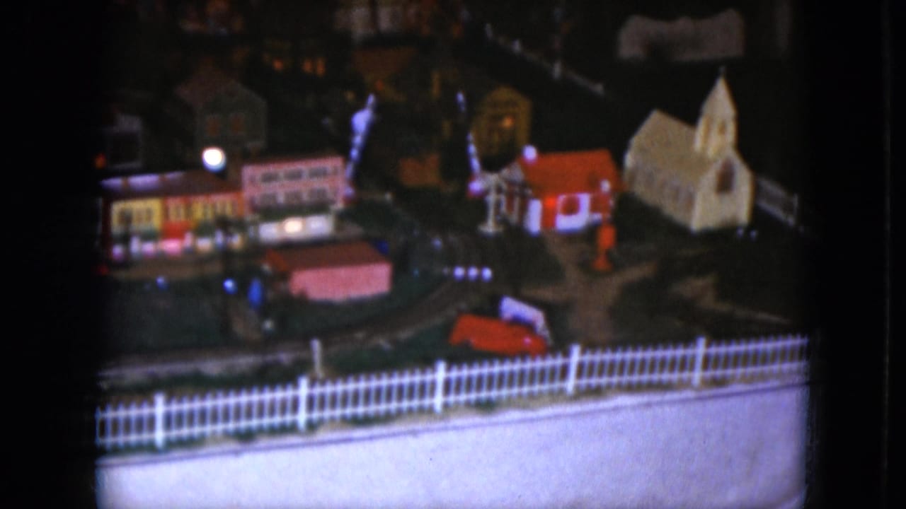 1951 Cleveland home-movie frame showing a lit model railroad town with small buildings, a church, and a white picket fence.