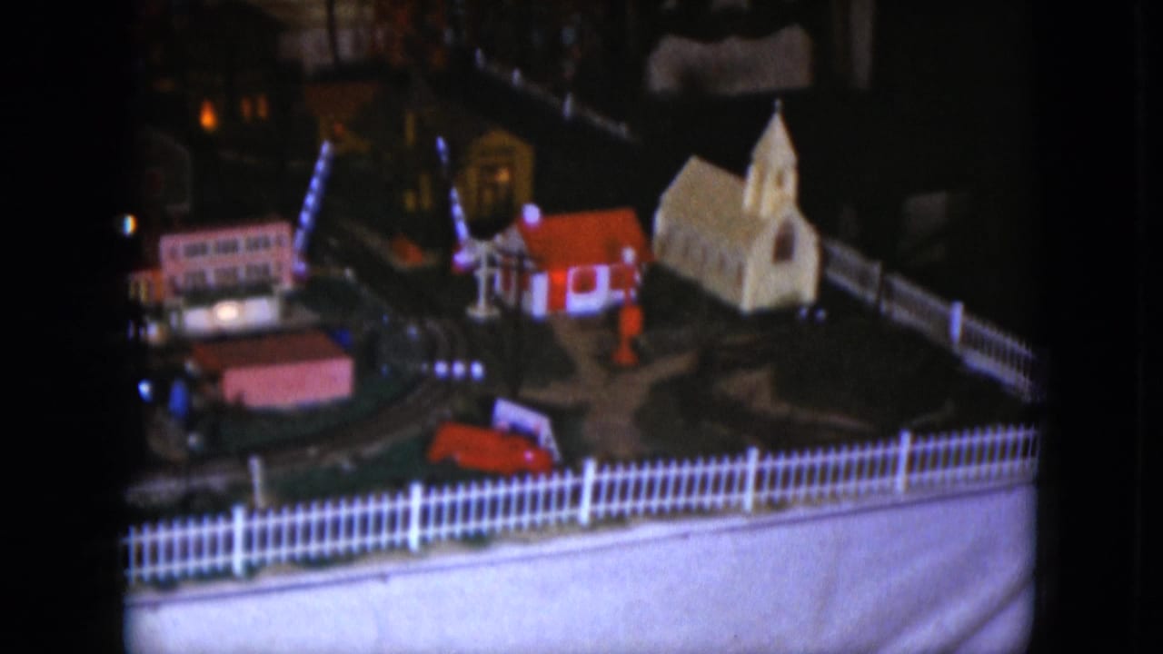 Lit 1951 miniature railroad display in Cleveland, with a small church, picket fence, and town buildings visible in soft focus.