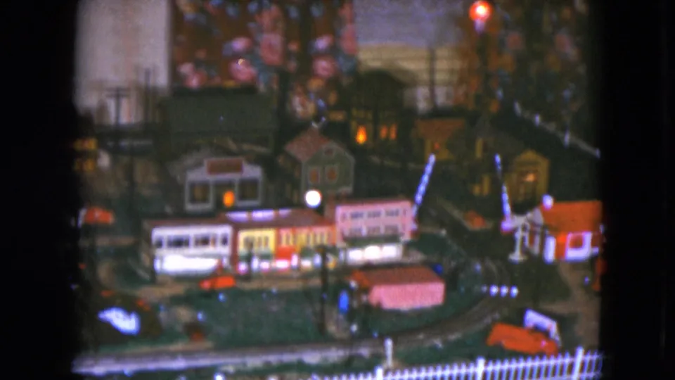 1951 Cleveland 8mm frame showing the model train city from a shifted angle, with train cars, storefronts, lamps, and a church.