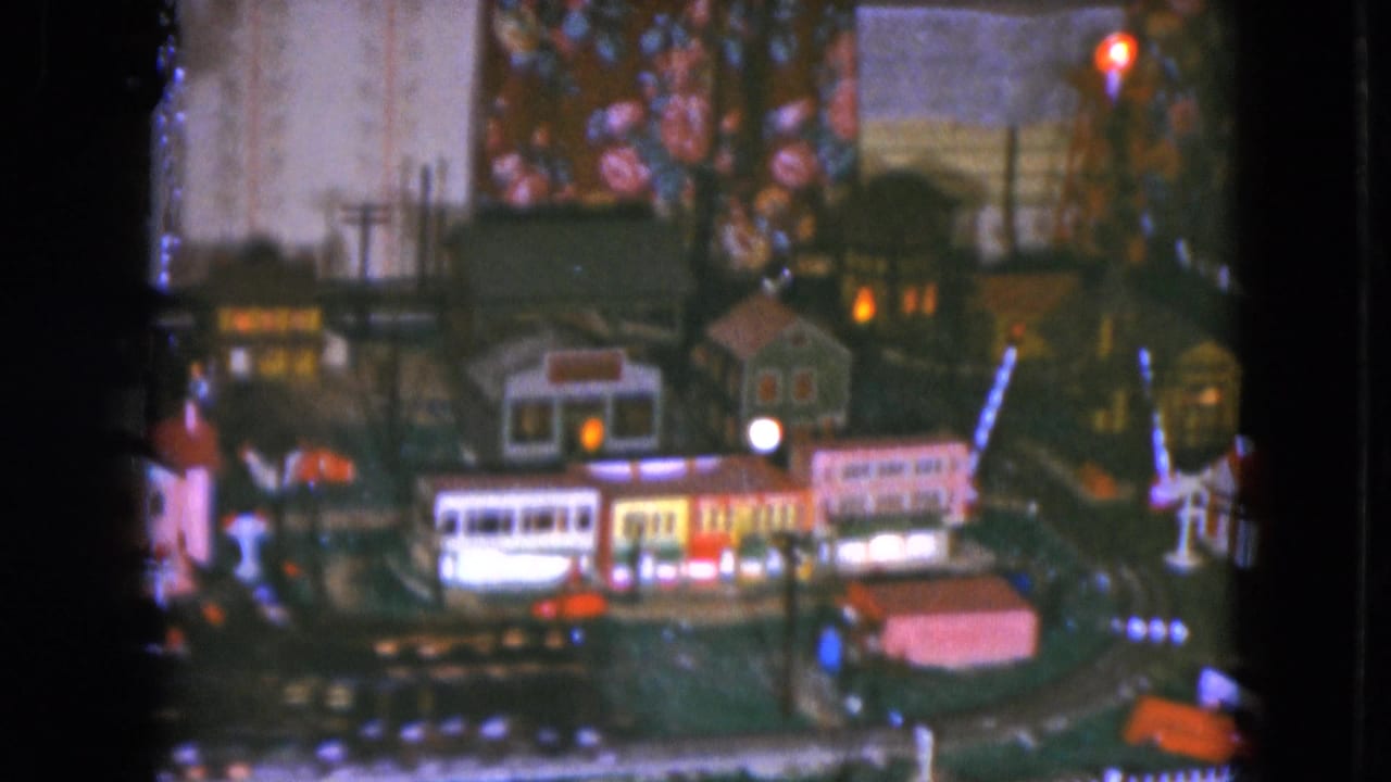 Miniature town with lit buildings, tracks, and Christmas tree decorations above.